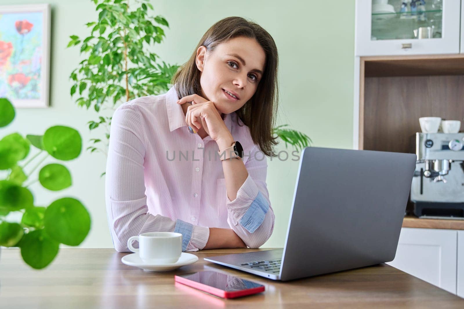 Smiling attractive young woman working at home using laptop, looking at camera. Lifestyle, freelancing, technology, job, work, leisure, people concept