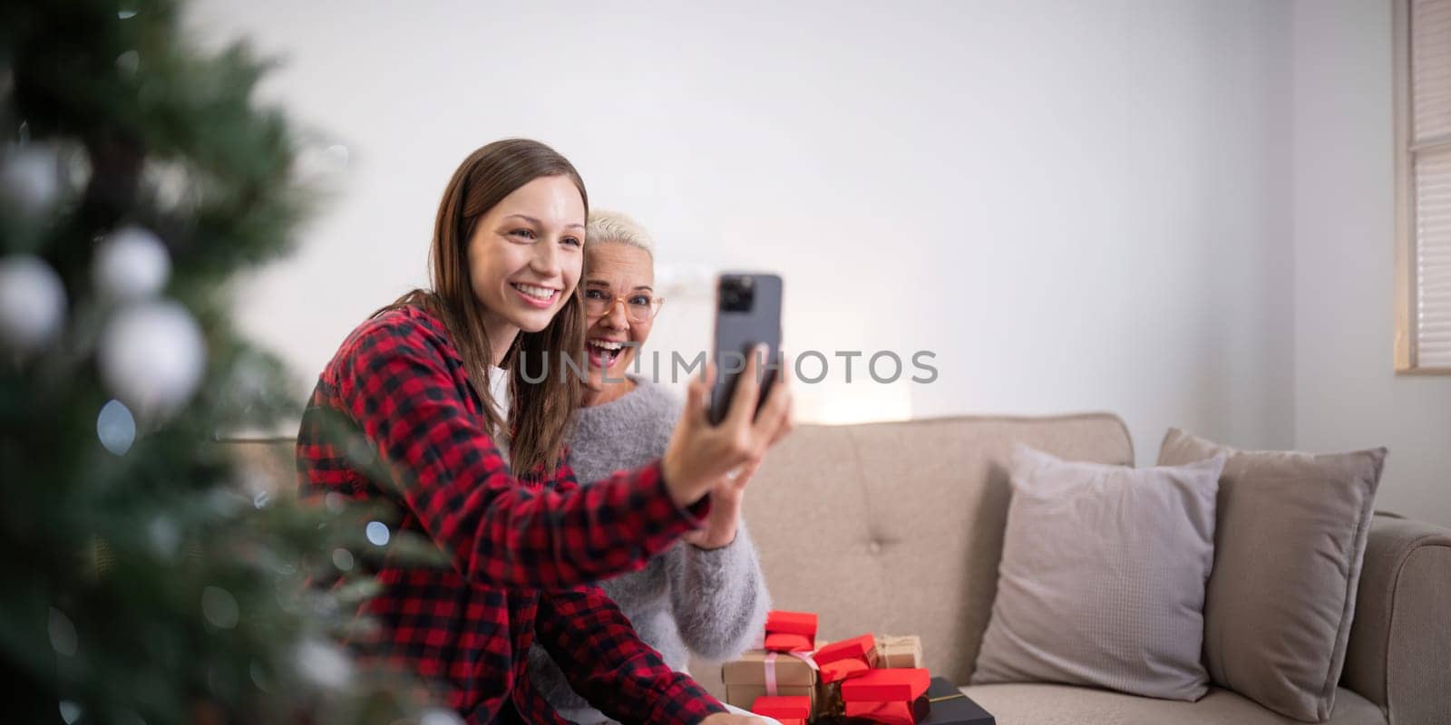 Cheerful daughter and mother celebrating christmas at home and with friend and family through a video call by nateemee