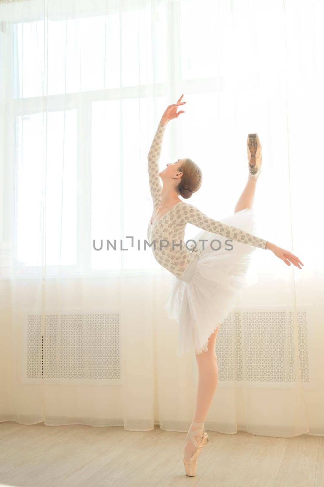 Beautiful ballerina in body and white tutu is training in a dance class. Young flexible dancer posing in pointe shoes. by mrwed54