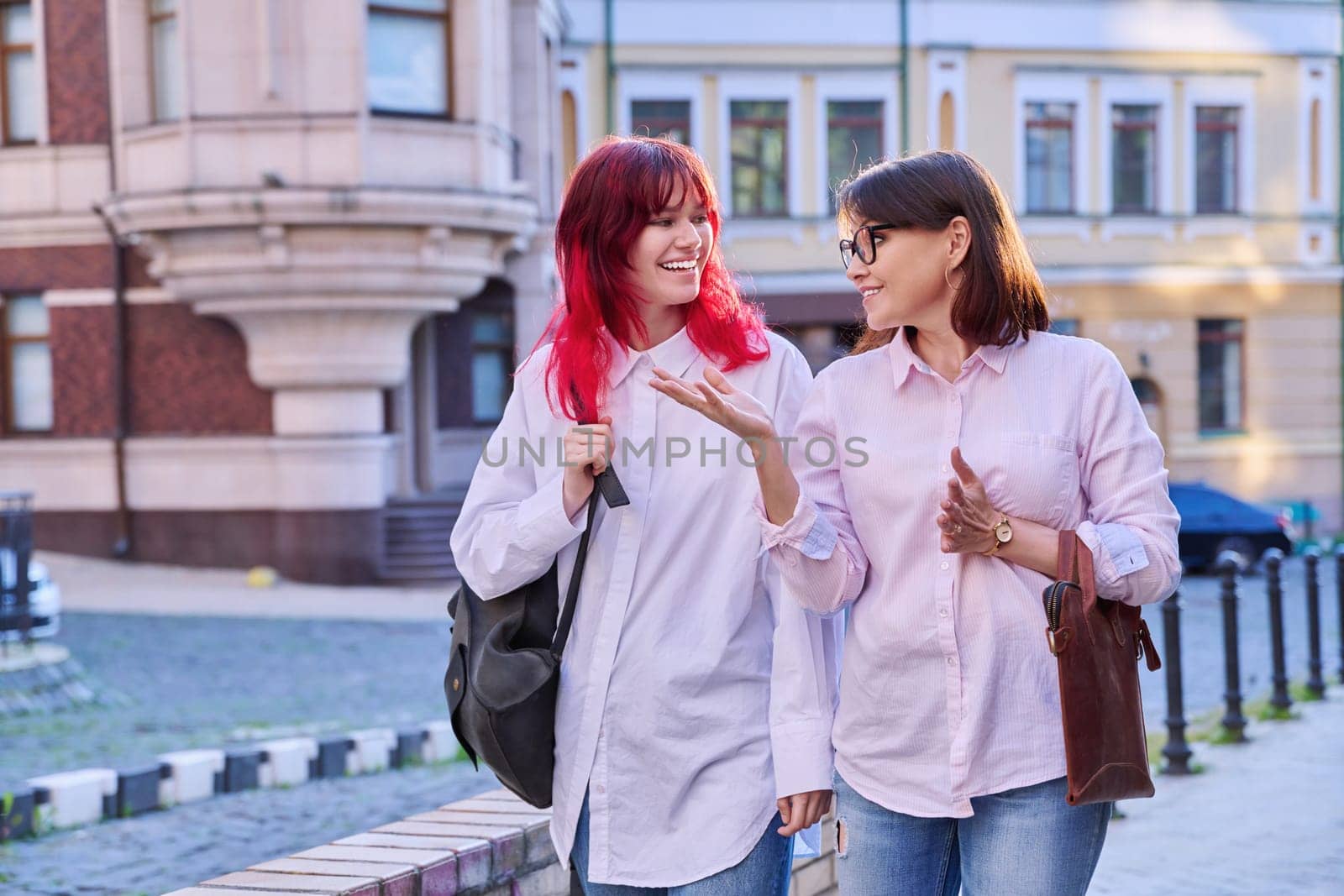 Mother and teenage daughter, walking talking together along city street by VH-studio