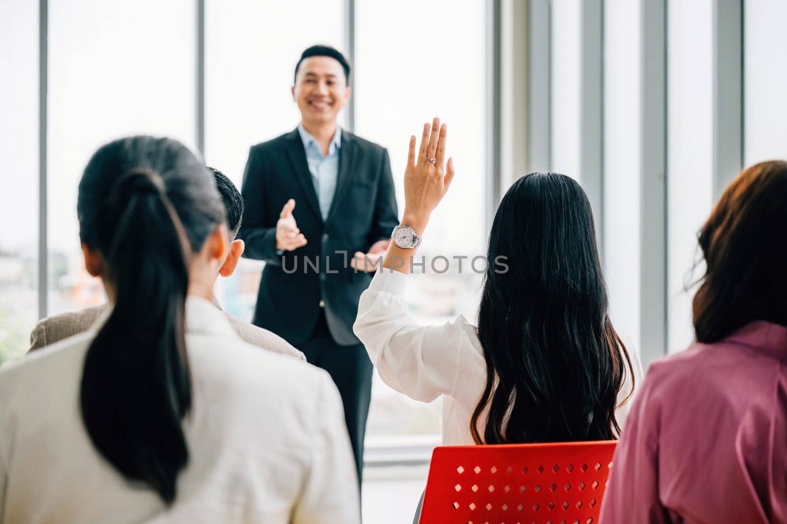 In a conference, business professionals raise their hands to ask questions, vote, or volunteer, highlighting teamwork and active audience involvement in a corporate setting.