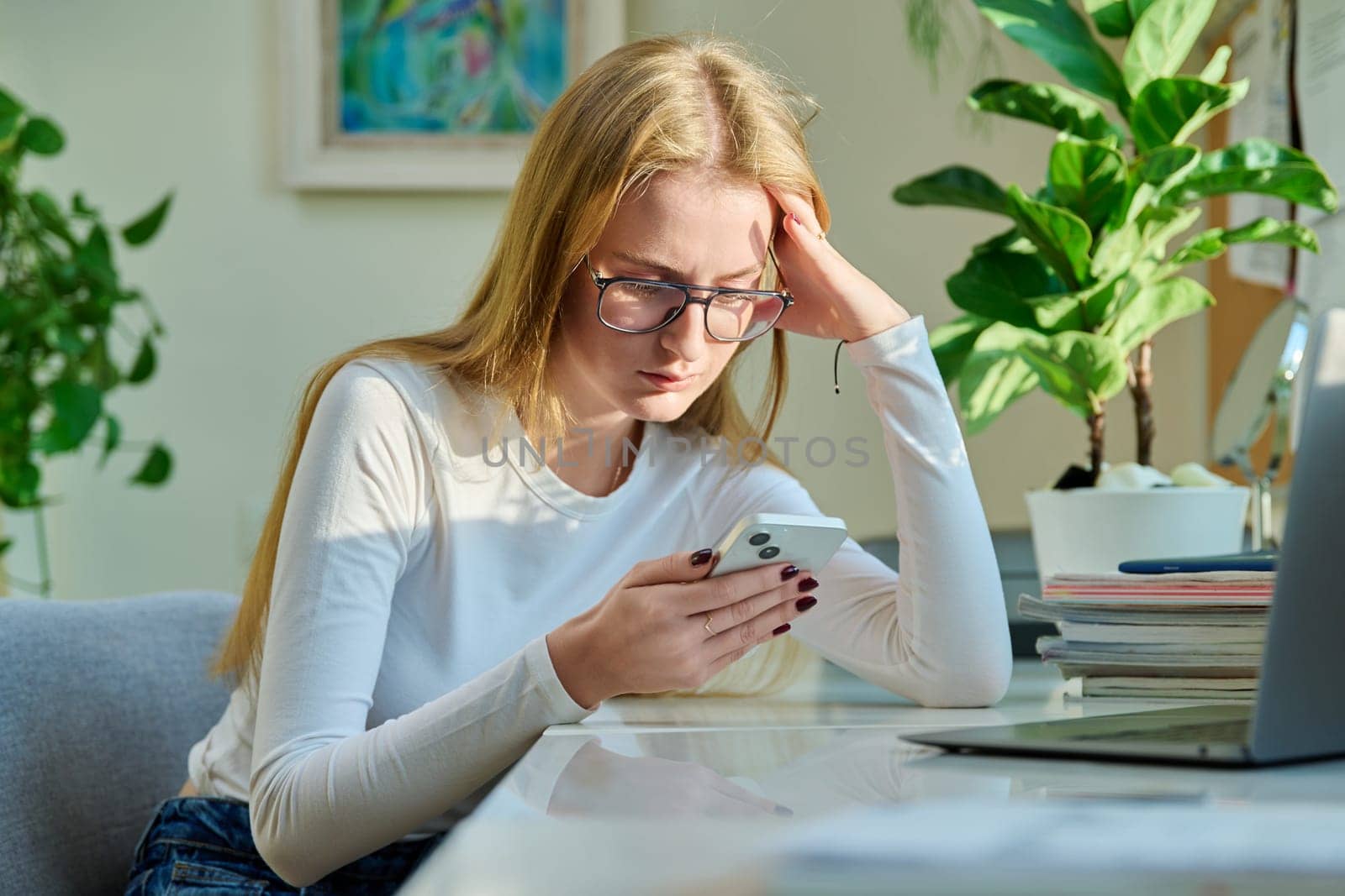 Serious sad teenage female sitting at home reading texting on smartphone. Social life, communication, study education, lifestyle technology concept