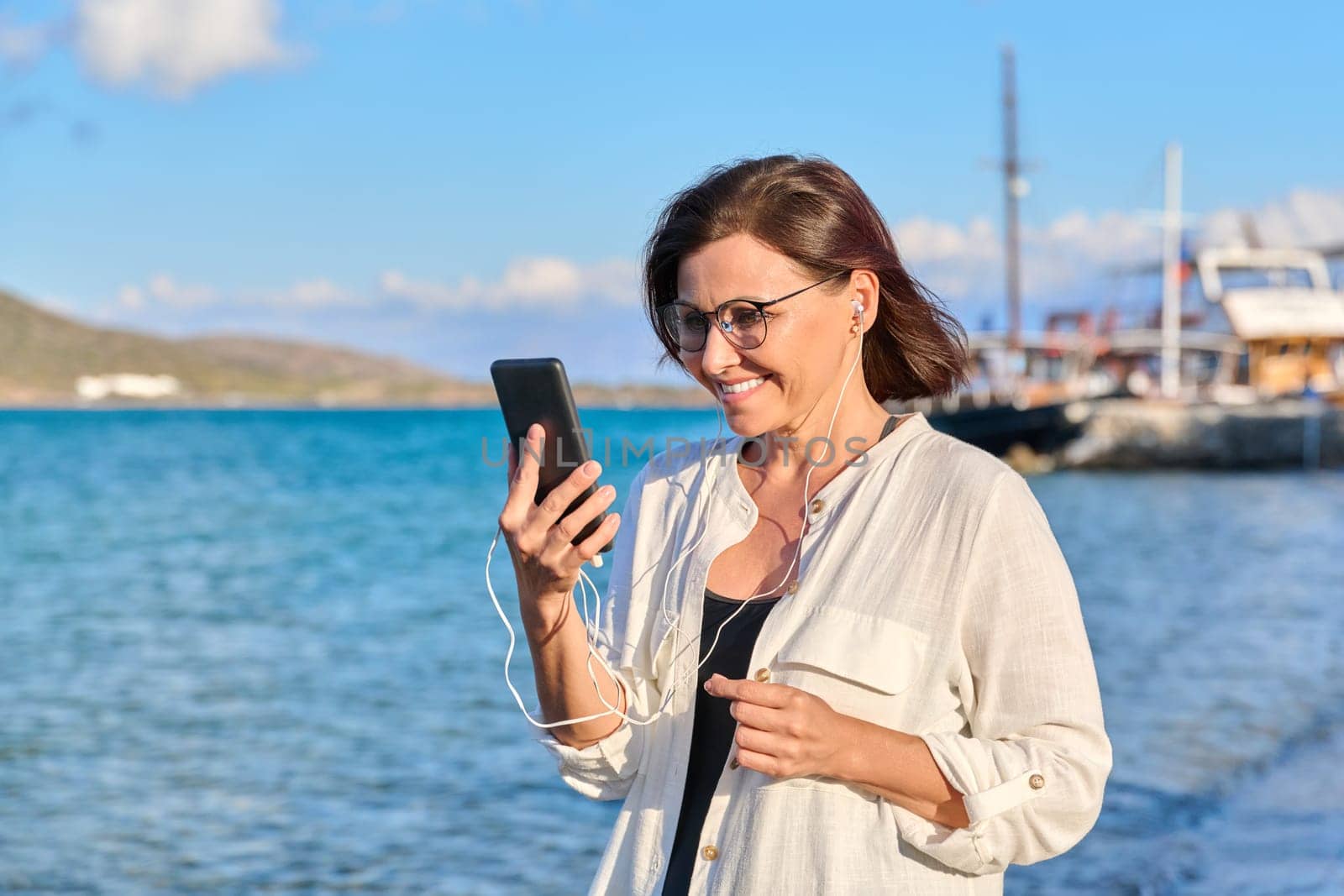 Happy 40s age woman in headphones with smartphone on the beach by VH-studio