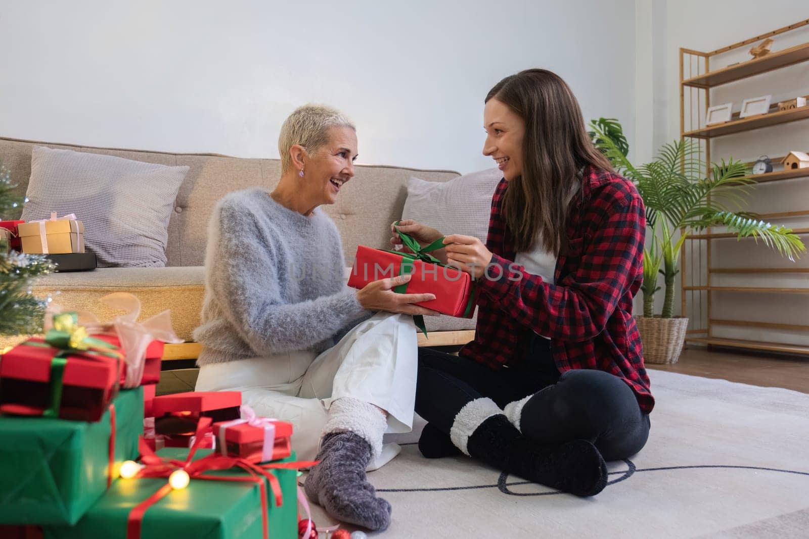 Cute young woman holds a gift box to surprise his mother on Christmas Day. 60 year old retired woman happy Happy daughter on Christmas day in living room holding red gift box.