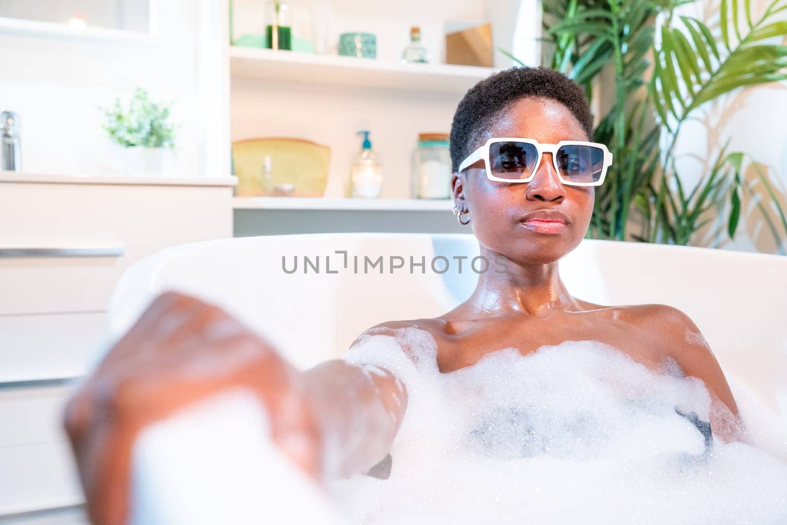 Attractive African woman in bathtub with sunglasses looking at camera. by PaulCarr