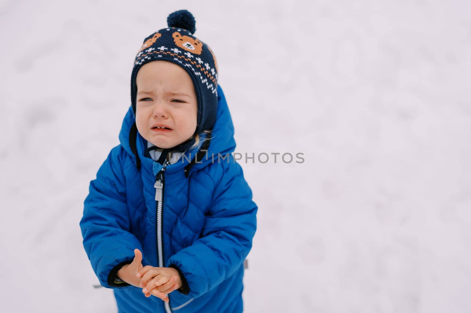 Little girl crying while standing in the snow and holding her hands in front of her by Nadtochiy