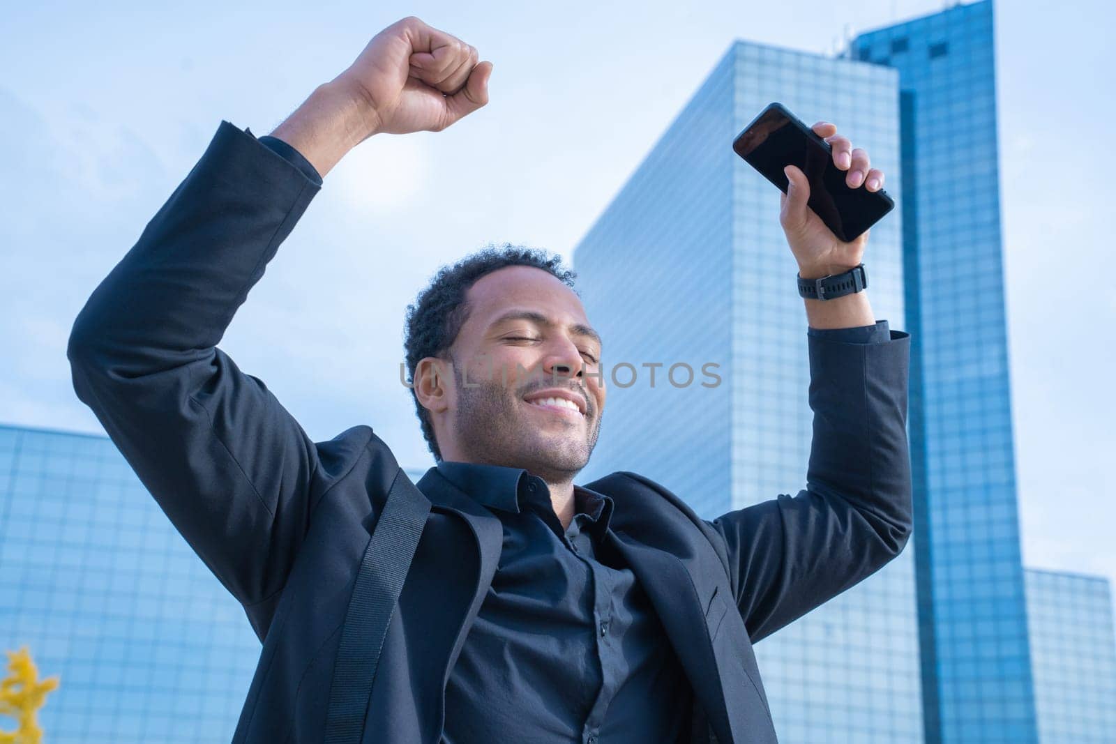 Happy businessman in suit with raised arms smiling celebrating success in the city. by PaulCarr
