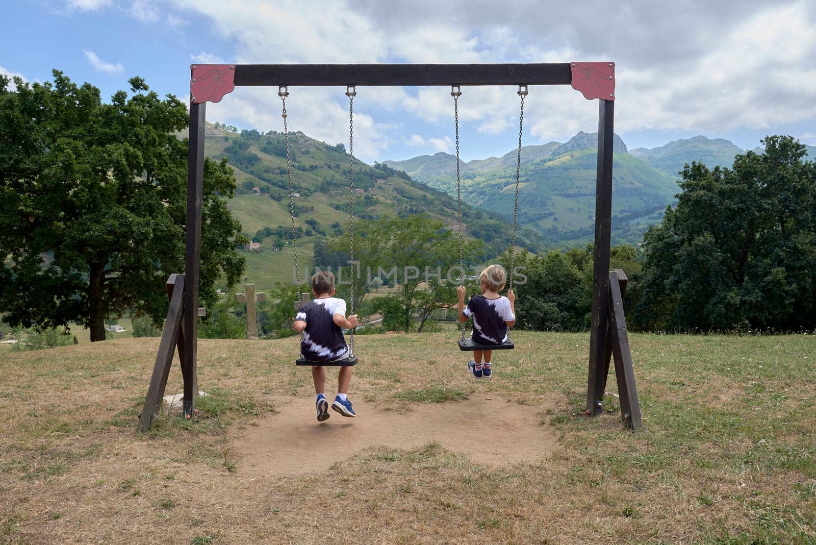Two children on their backs swinging towards the mountain.Caucasian, vegetation swing, not recognisable, ribio, chestnut, sportswear alike