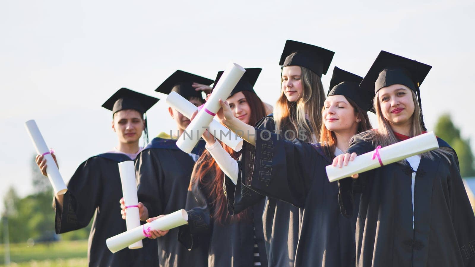 Cheerful graduates waving their diplomas on a sunny day