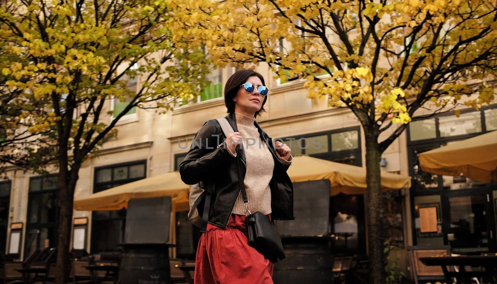 Attractive Woman In Sunglasses Walks By City Street With Backpack, Radiating Confidence And Style