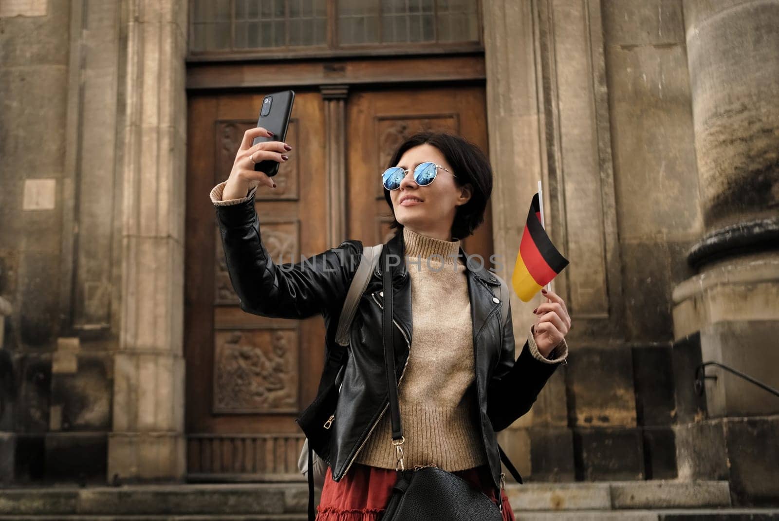 Attractive Female Tourist Walks With Germany Flag In Historical Center Of Dresden, Taking A Selfie