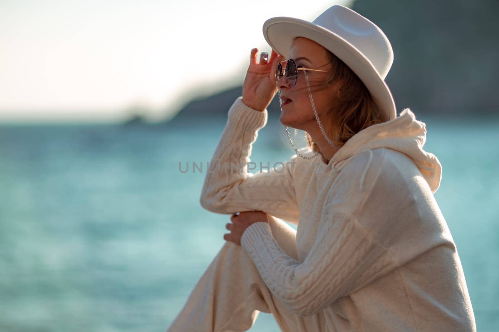 Happy blonde woman in a white suit and hat posing at the camera against the backdrop of the sea by Matiunina