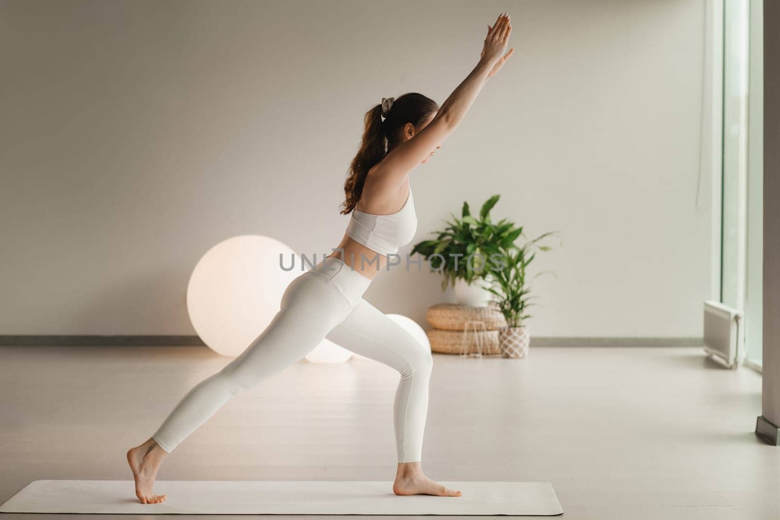 A girl in white clothes does yoga on a mat indoors.