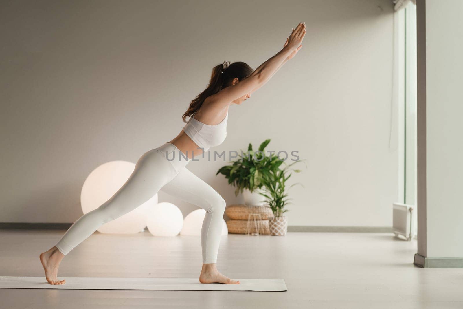 A girl in white clothes does yoga on a mat indoors.