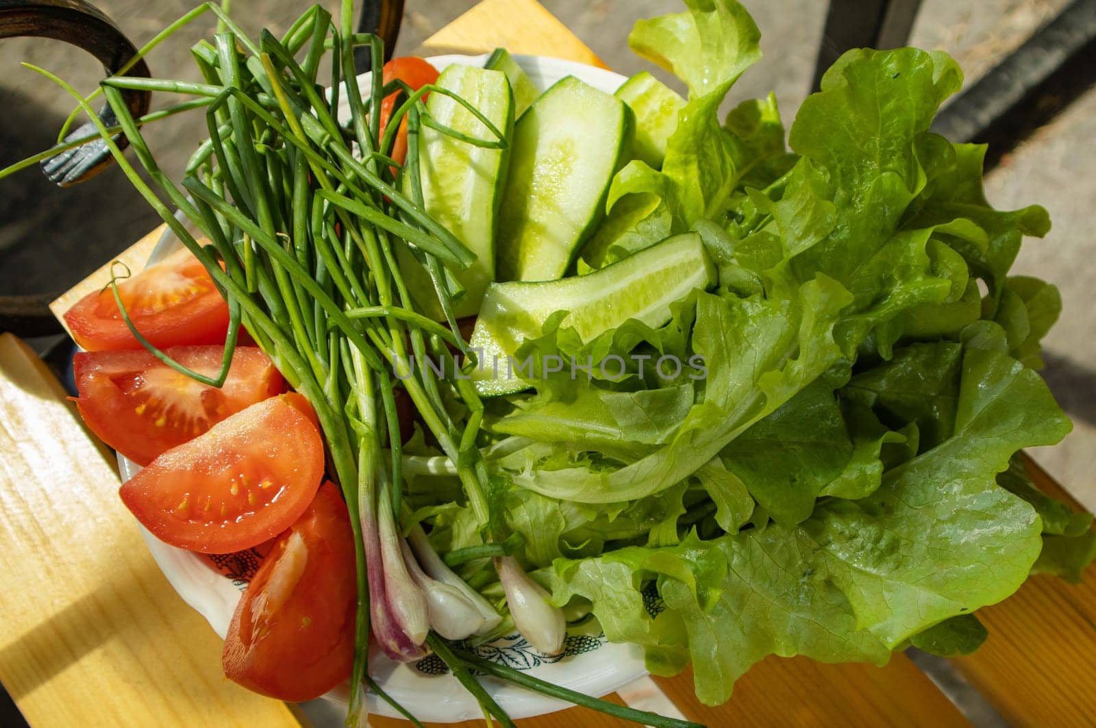 Fresh vegetables - lettuce, green onion, tomatoes and cucumbers on a white plate on a wooden background. The concept of cooking healthy food. View from above.