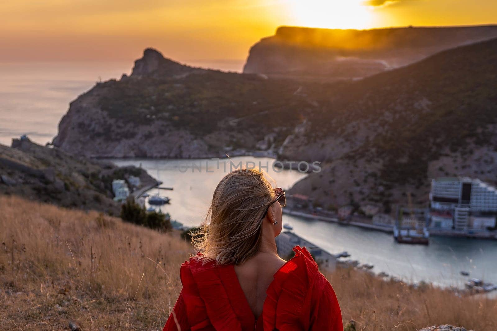 Woman sunset sea mountains. Happy woman siting with her back on the sunset in nature summer posing with mountains on sunset, silhouette. Woman in the mountains red dress, eco friendly, summer landscape active rest by Matiunina