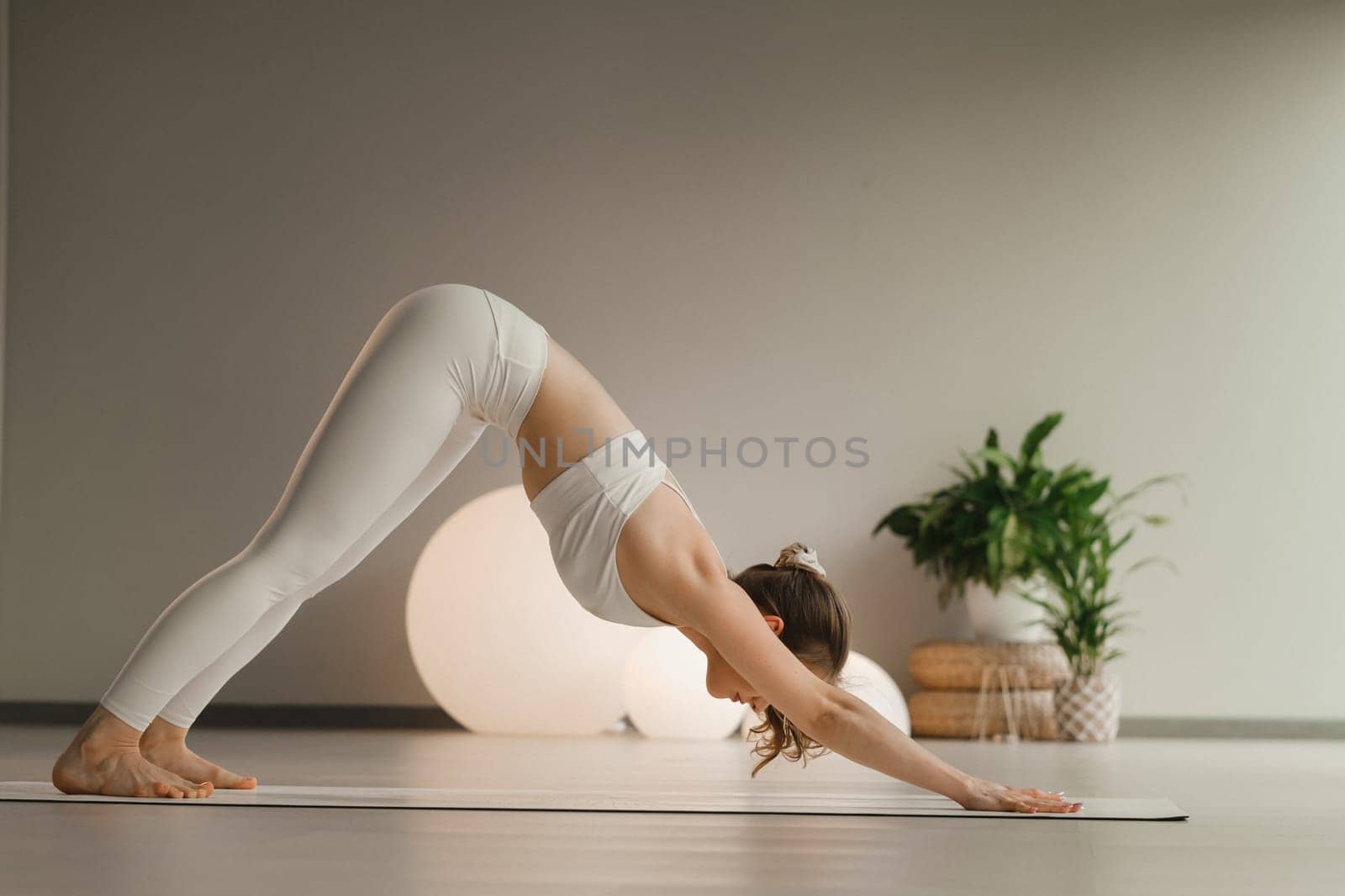 A girl in white clothes does yoga on a mat indoors.