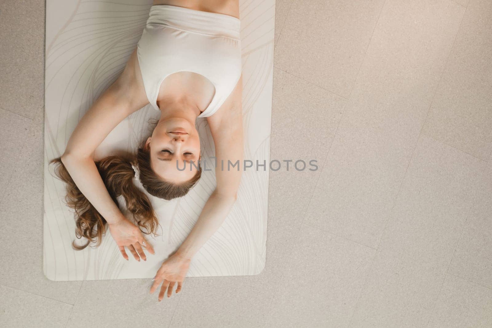 A girl in white clothes does yoga lying on a rug indoors.