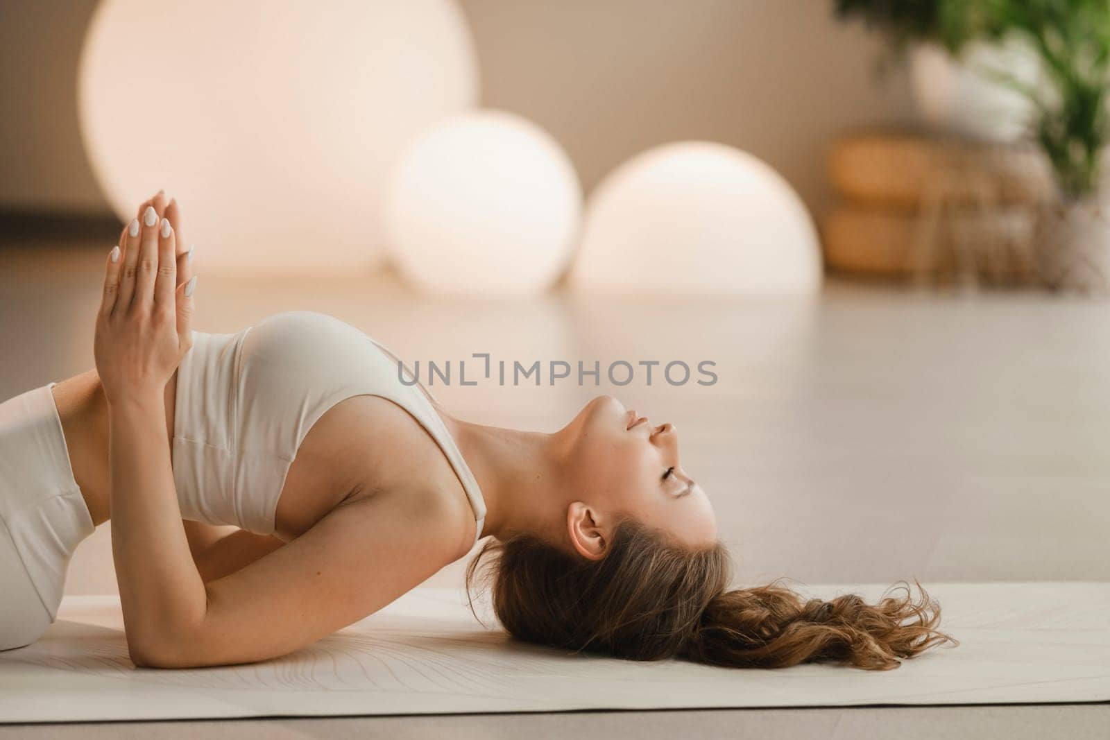 A girl in white clothes does yoga lying on a rug indoors.