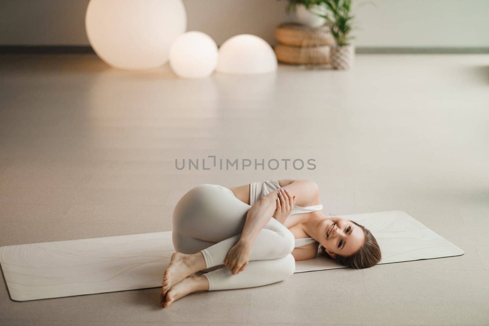 A girl in white clothes does yoga lying on a rug indoors.