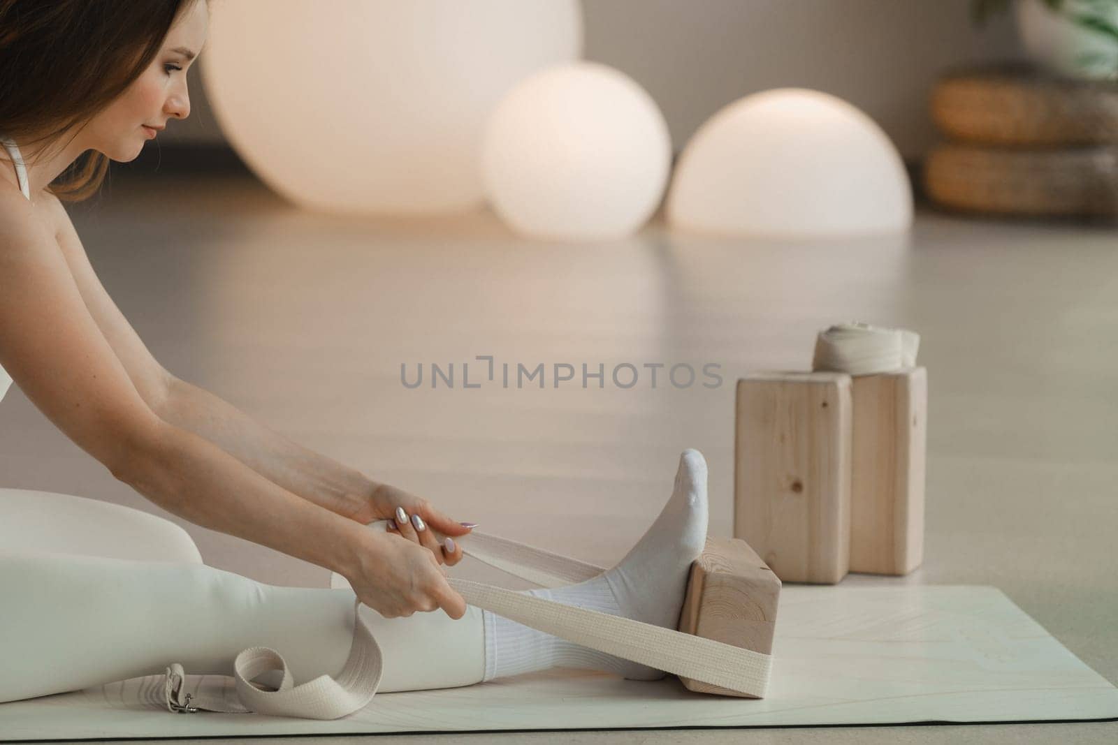 A girl does yoga with a support block sitting on a mat indoors.