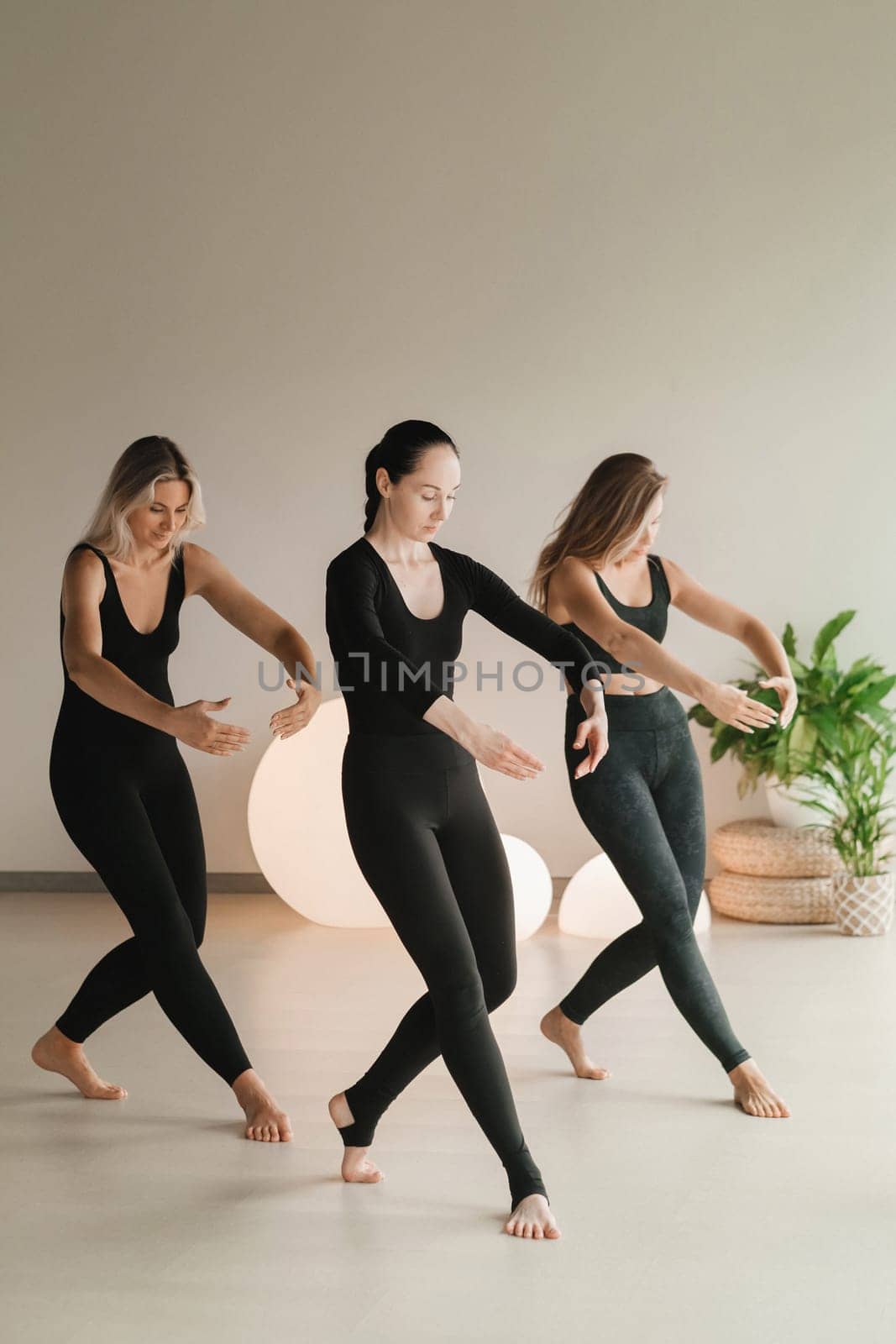 A group of girls in black doing yoga poses indoors. Women are engaged in fitness by Lobachad