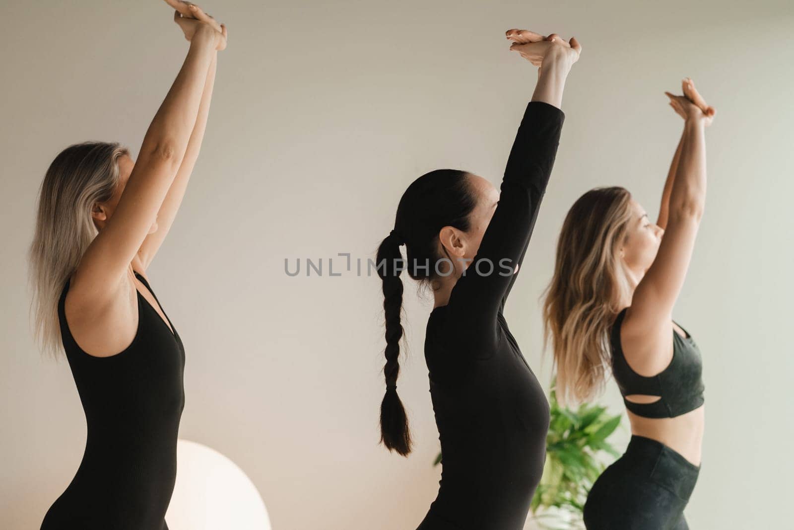 A group of girls in black doing yoga poses indoors. Women are engaged in fitness by Lobachad