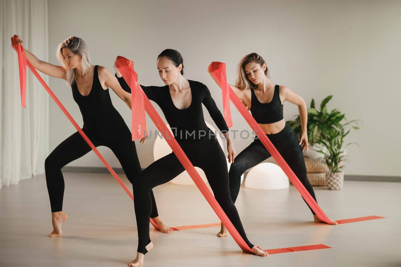 Girls in black are doing fitness with red ribbons indoors.