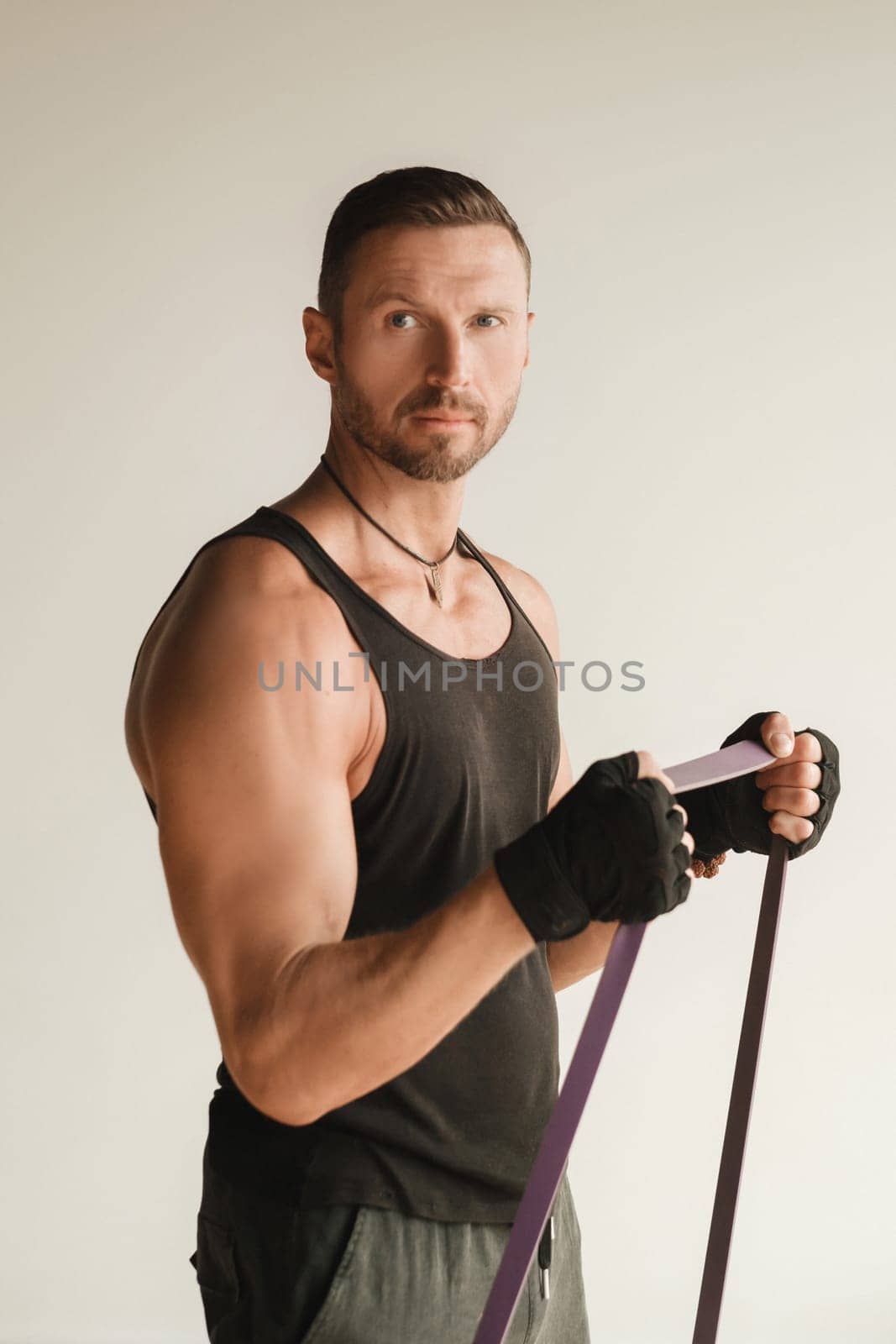 A man in black sportswear is engaged in strength fitness using a rubber loop indoors by Lobachad