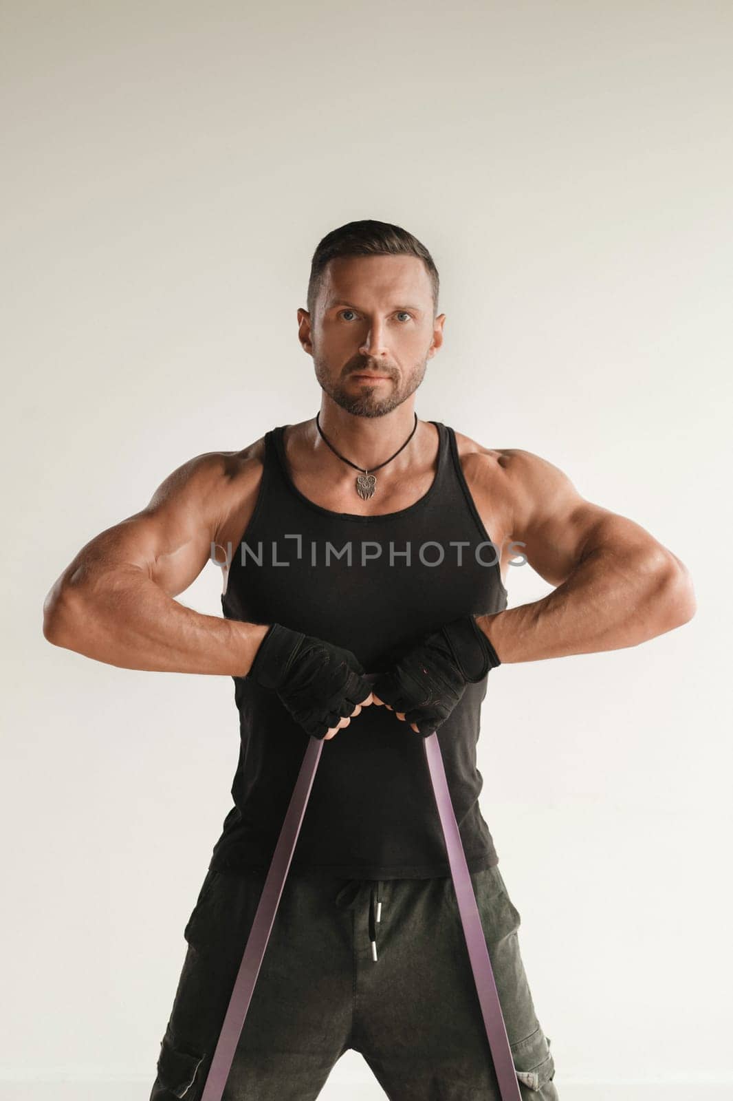 A man in black sportswear is engaged in strength fitness using a rubber loop indoors.