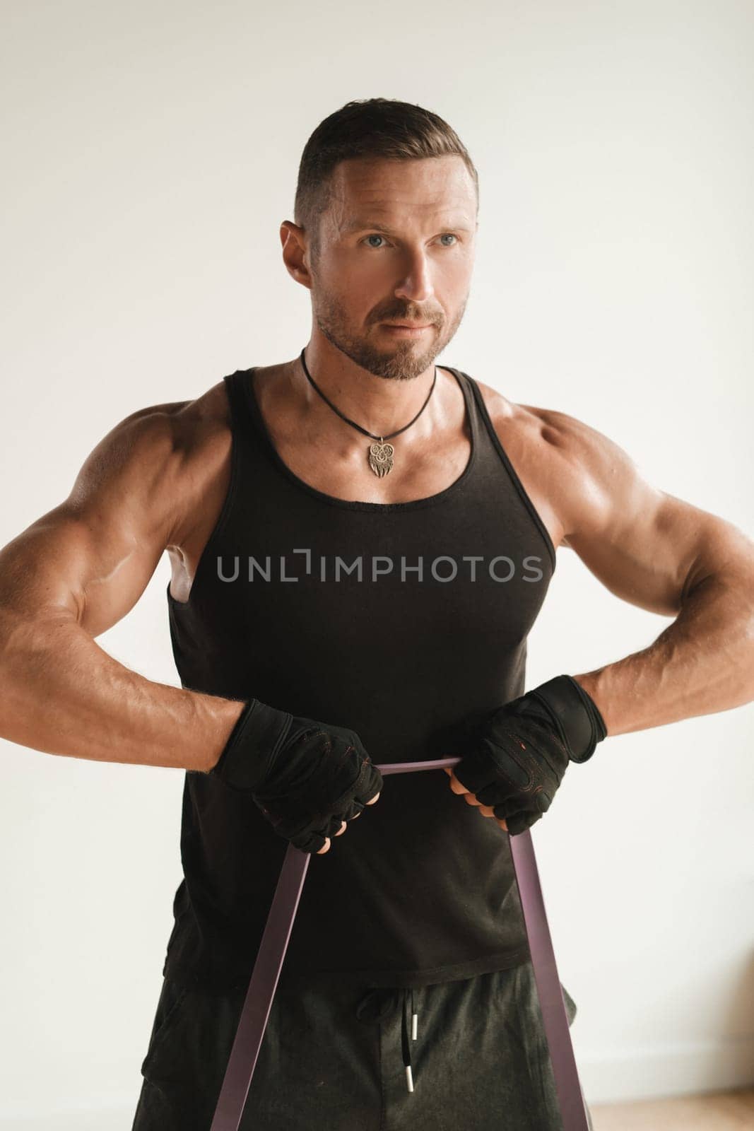 A man in black sportswear is engaged in strength fitness using a rubber loop indoors.