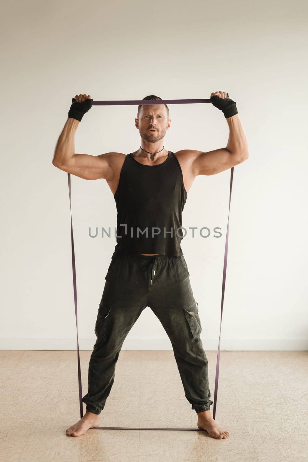 A man in black sportswear is engaged in strength fitness using a rubber loop indoors.