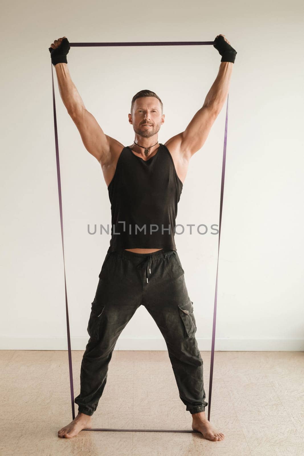 A man in black sportswear is engaged in strength fitness using a rubber loop indoors by Lobachad