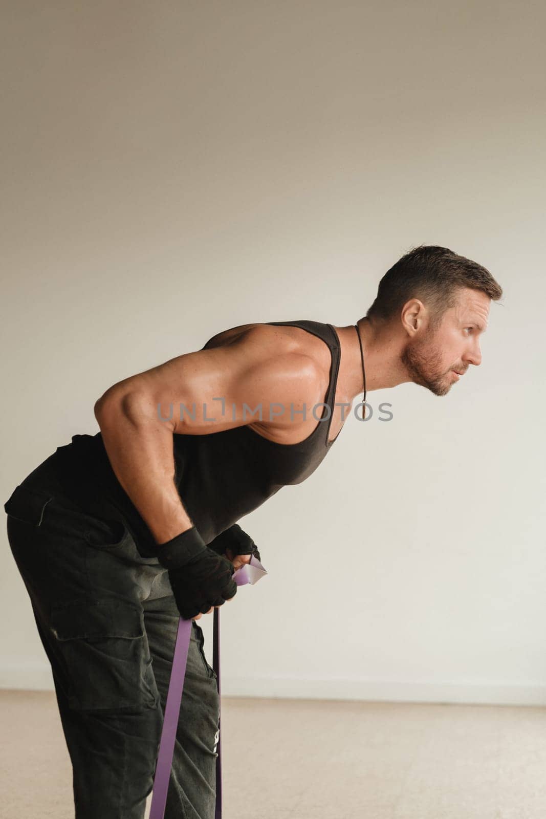 A man in black sportswear is engaged in strength fitness using a rubber loop indoors.