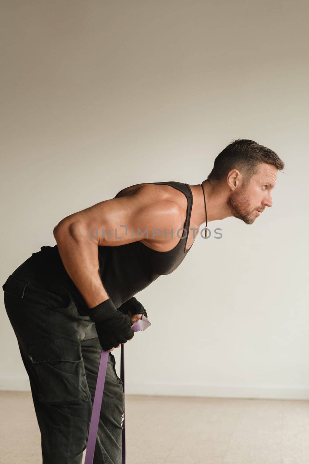 A man in black sportswear is engaged in strength fitness using a rubber loop indoors by Lobachad