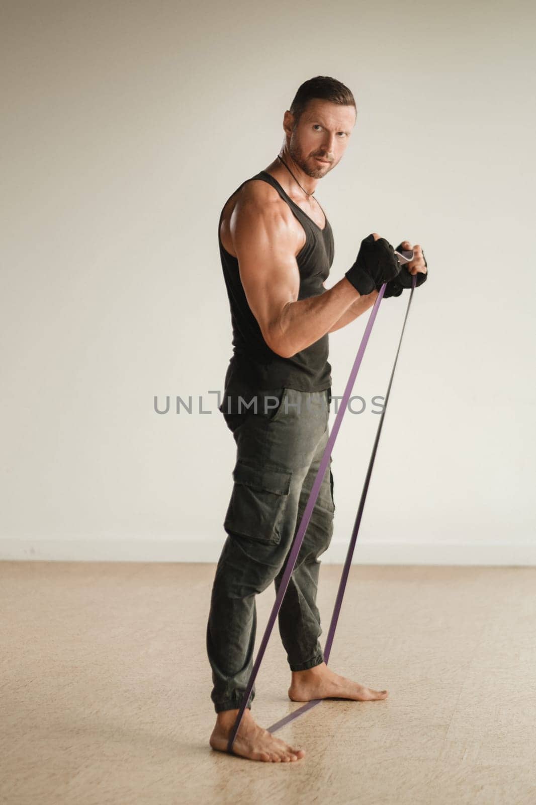 A man in black sportswear is engaged in strength fitness using a rubber loop indoors.