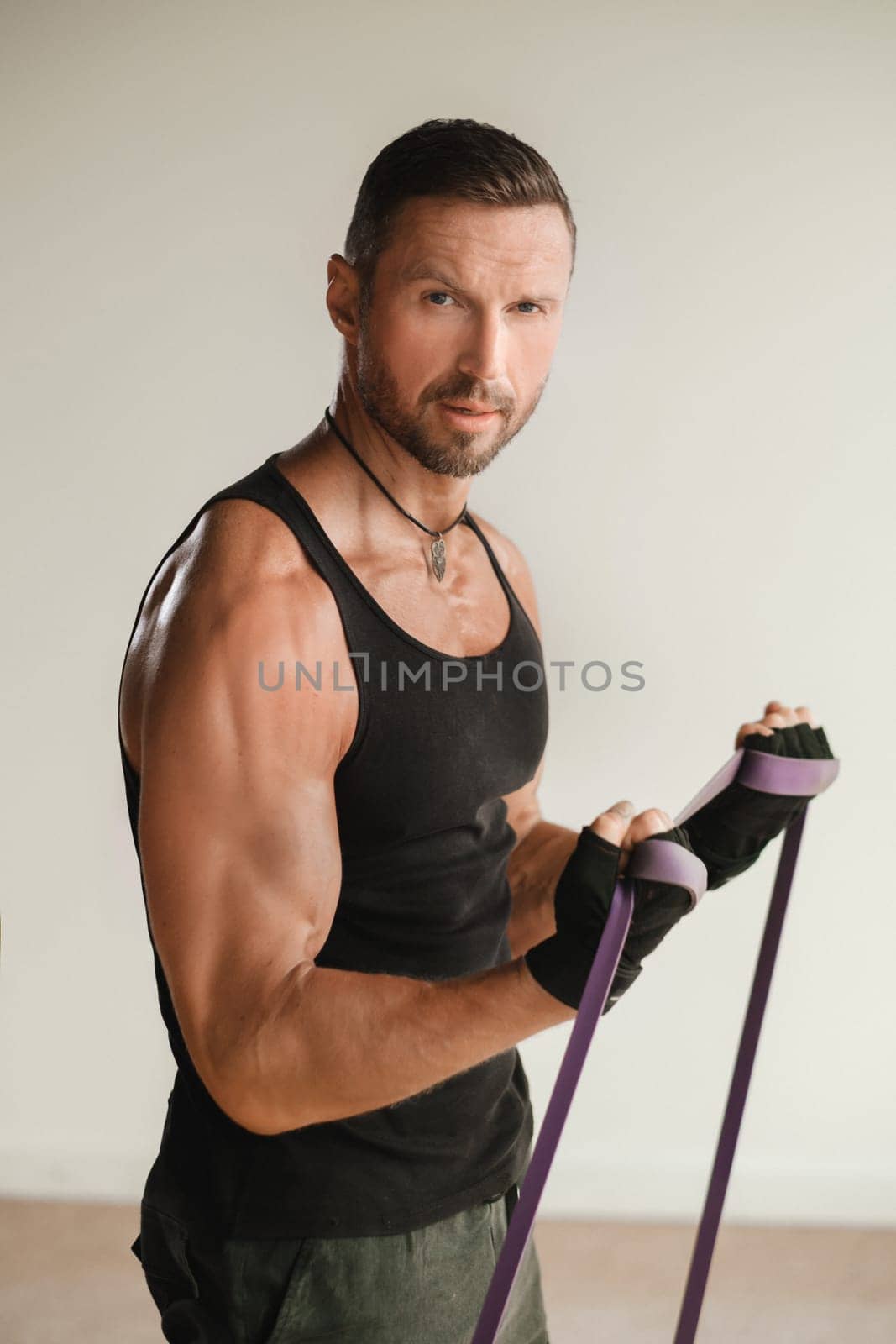 A man in black sportswear is engaged in strength fitness using a rubber loop indoors.