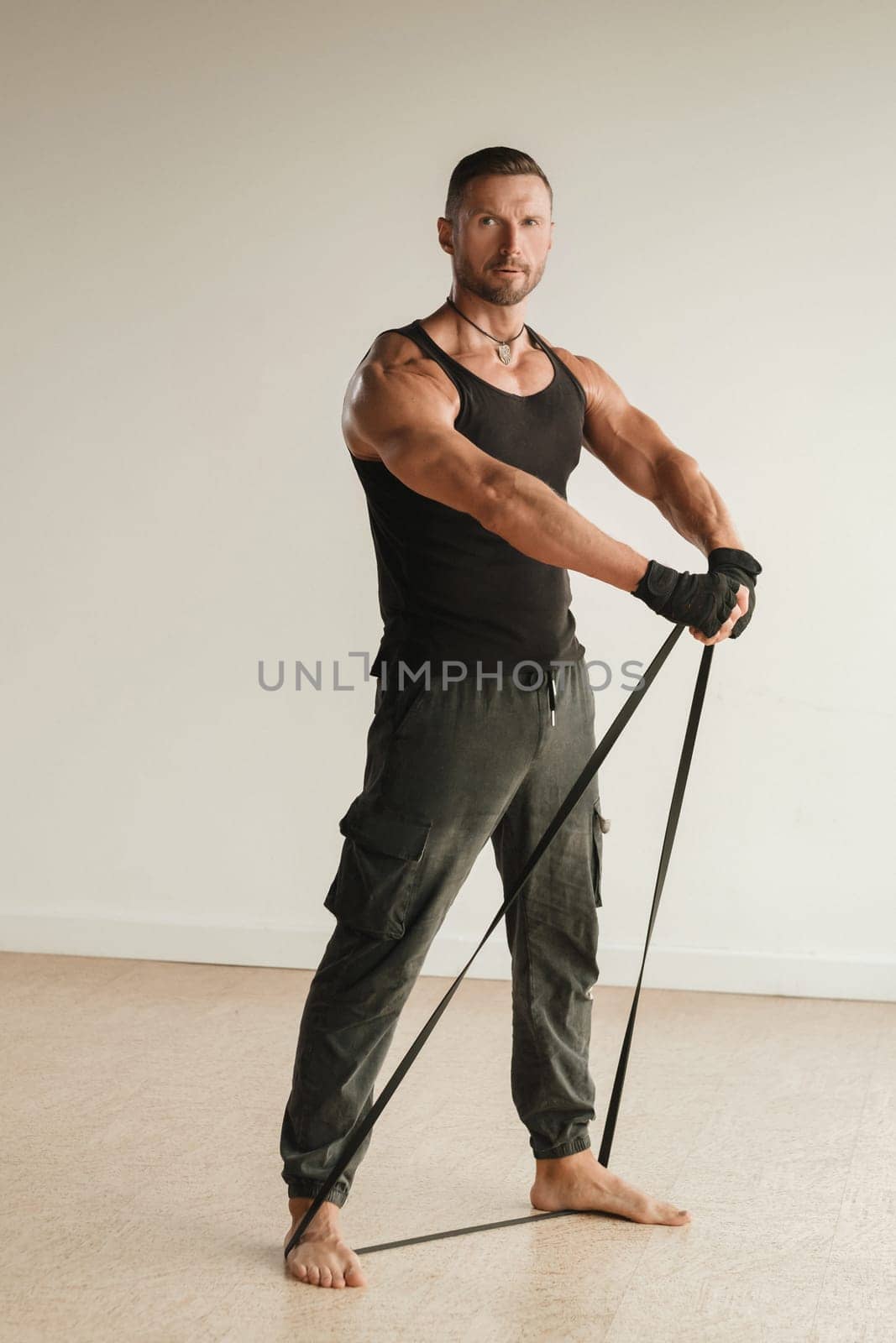 A man in black sportswear is engaged in strength fitness using a rubber loop indoors by Lobachad