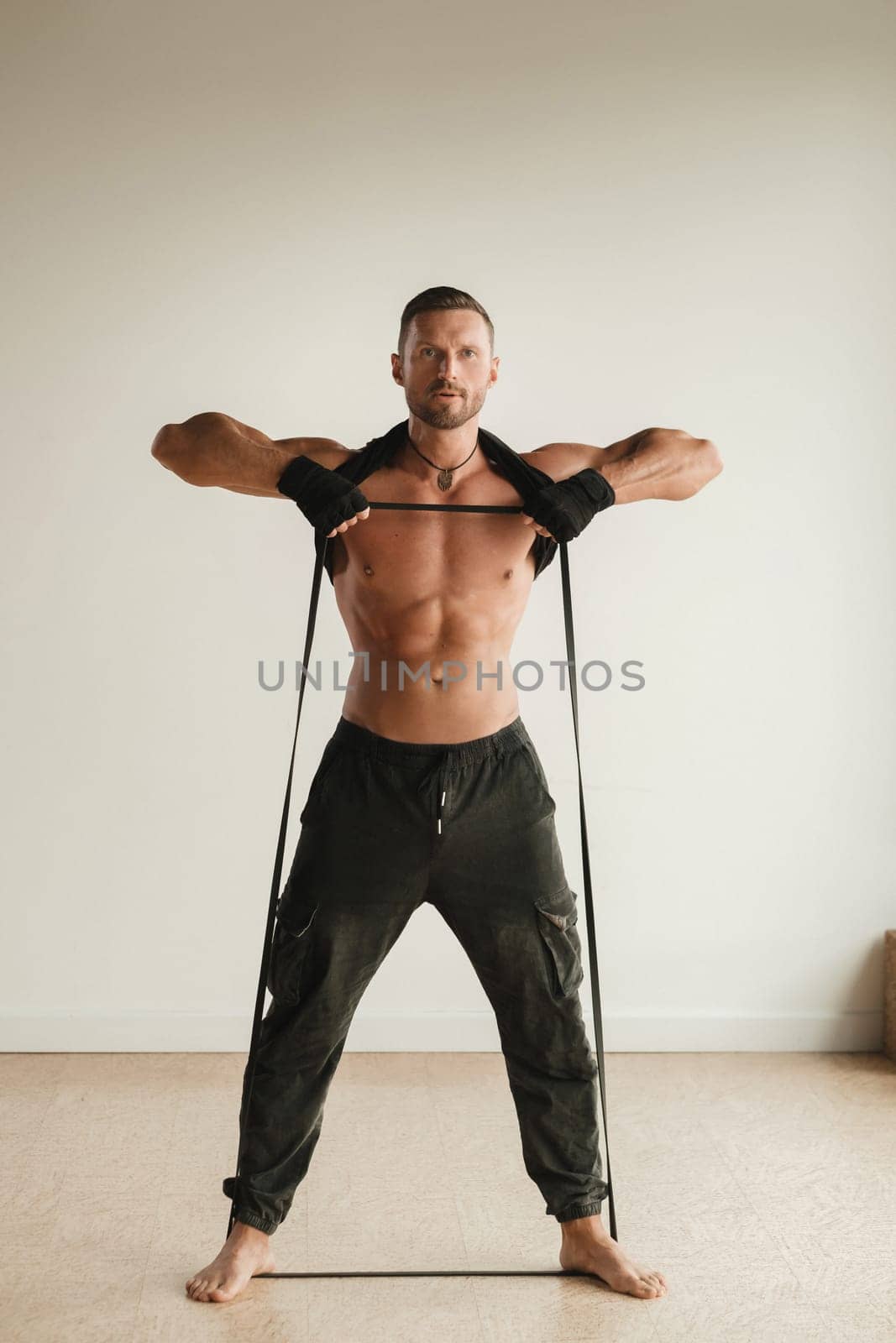 A man with a naked torso is engaged in strength fitness using a rubber loop indoors.