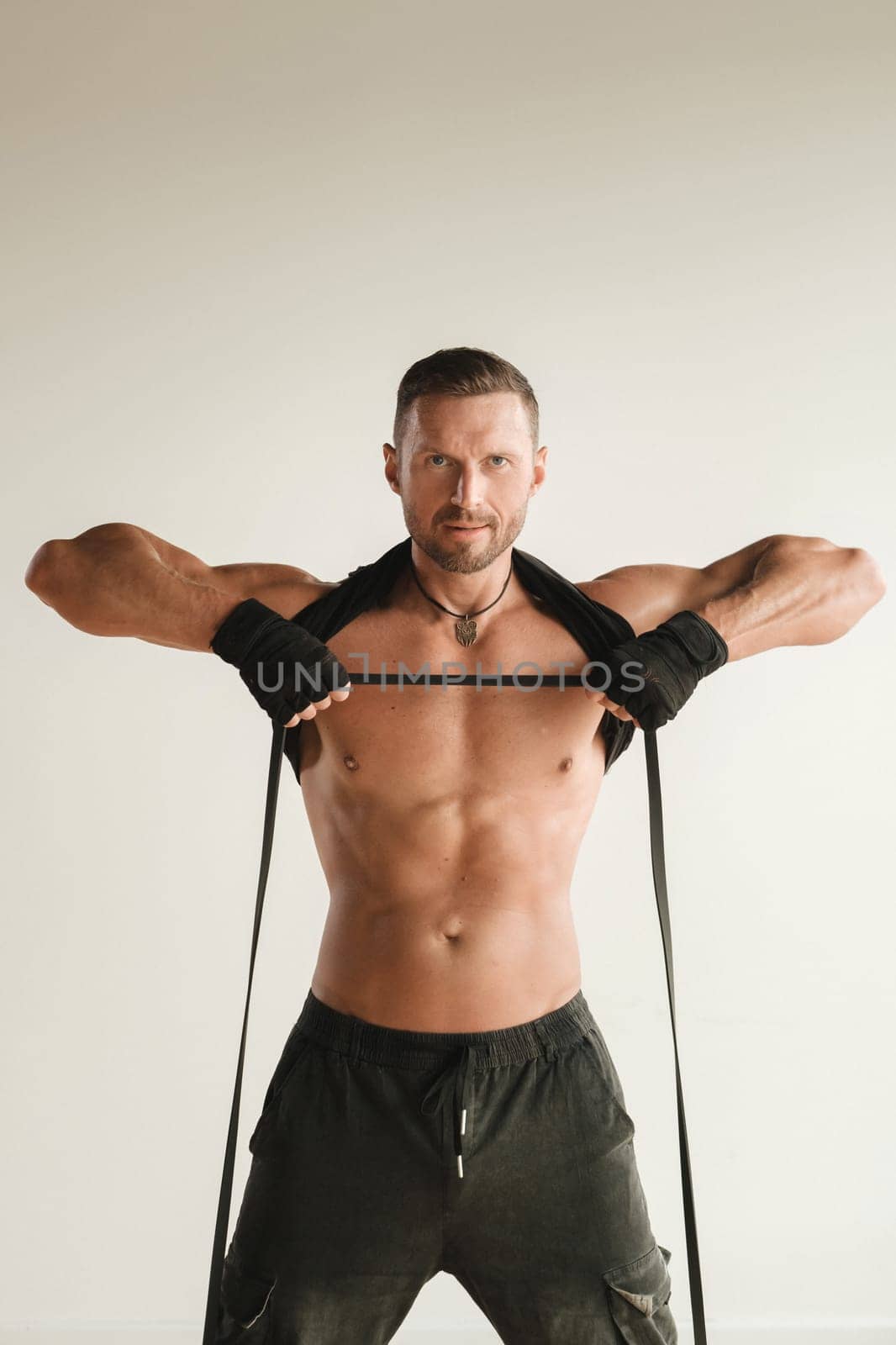 A man with a naked torso is engaged in strength fitness using a rubber loop indoors.