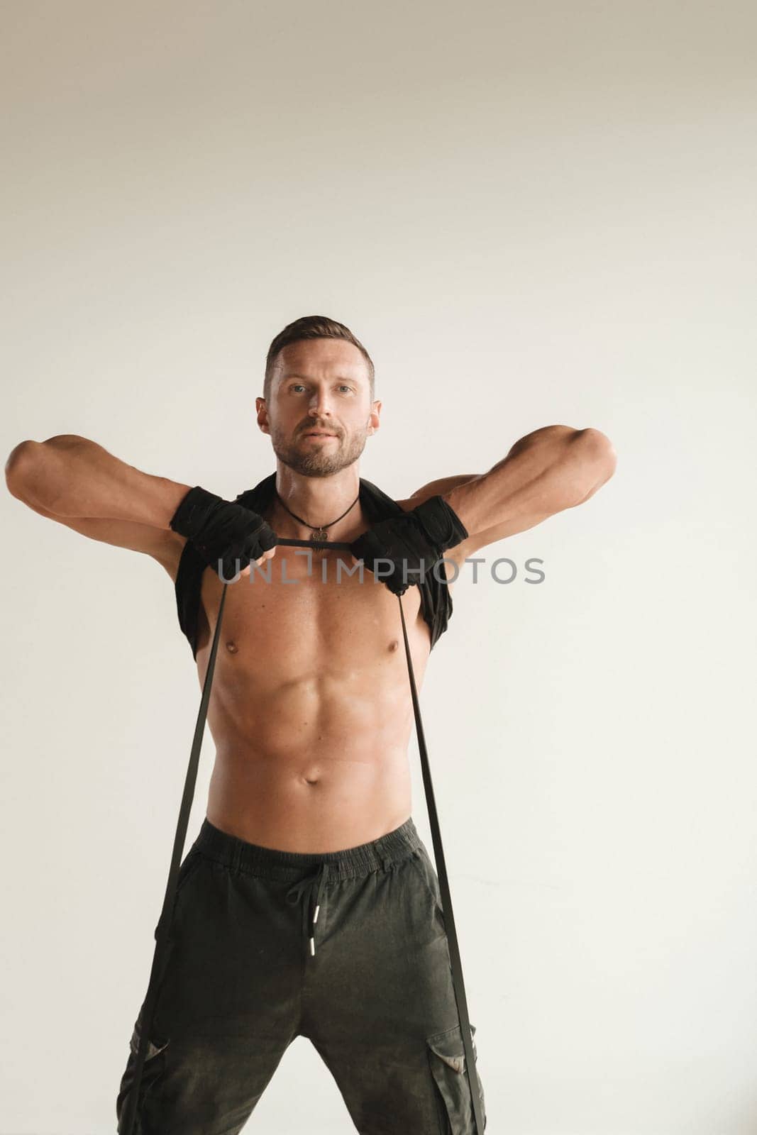 A man with a naked torso is engaged in strength fitness using a rubber loop indoors.