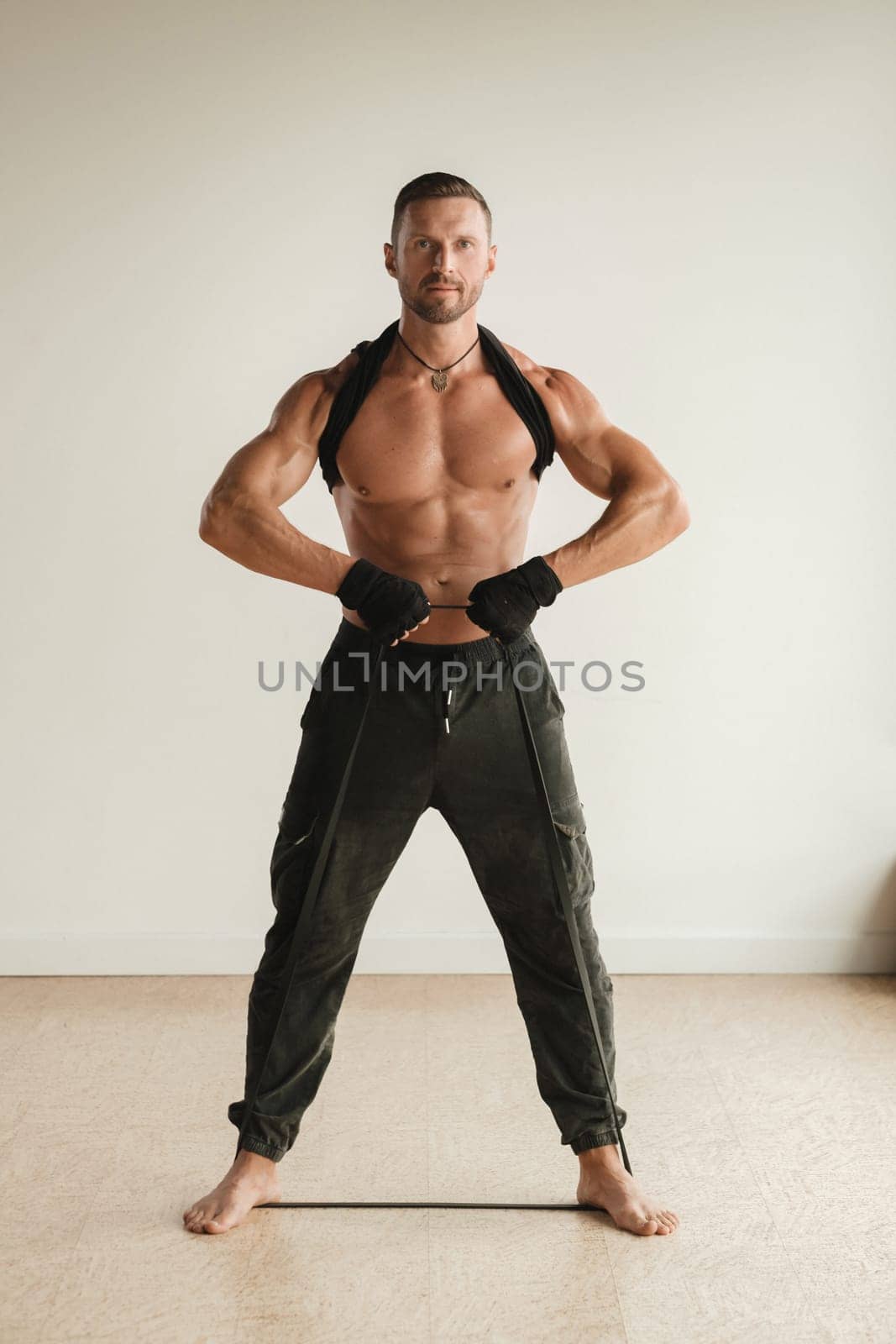 A man with a naked torso is engaged in strength fitness using a rubber loop indoors by Lobachad