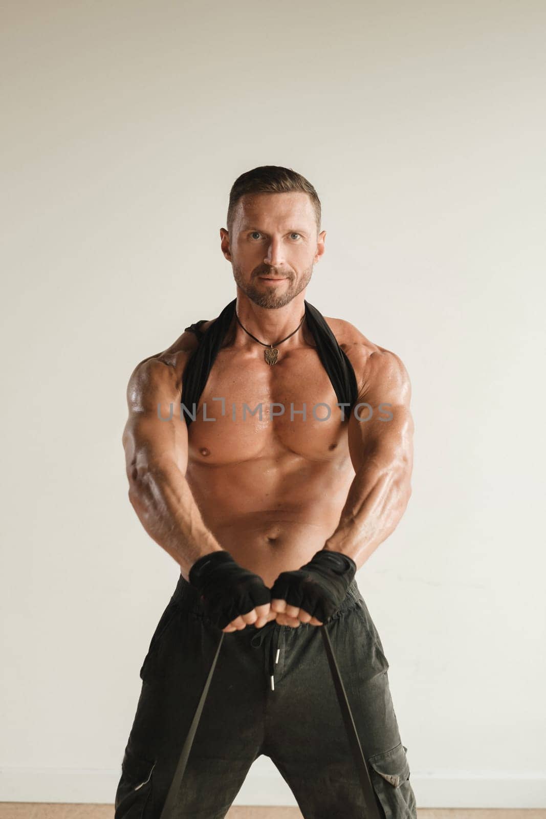 A man with a naked torso is engaged in strength fitness using a rubber loop indoors by Lobachad