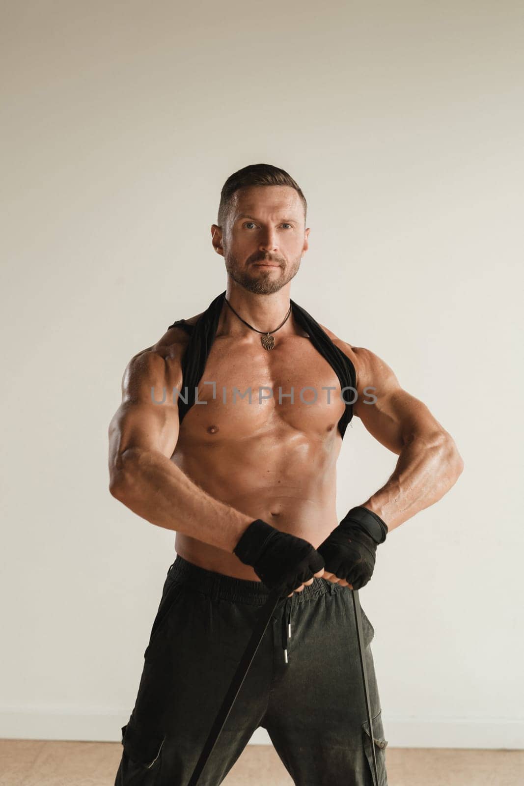 A man with a naked torso is engaged in strength fitness using a rubber loop indoors.