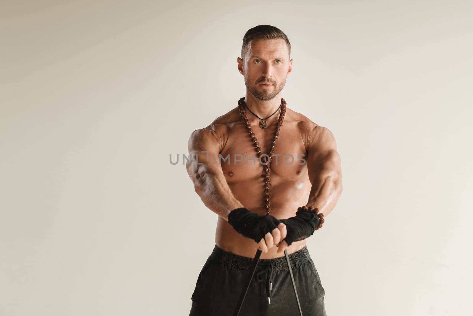 A man with a naked torso is engaged in strength fitness using a rubber loop indoors.