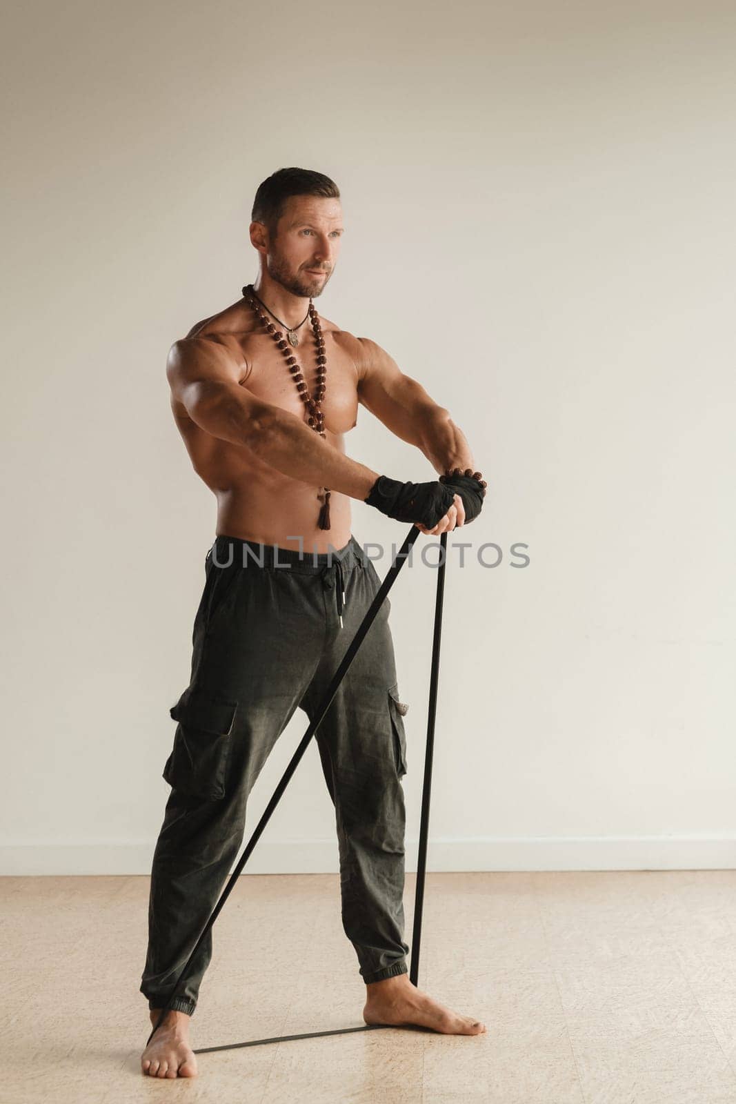 A man with a naked torso is engaged in strength fitness using a rubber loop indoors.