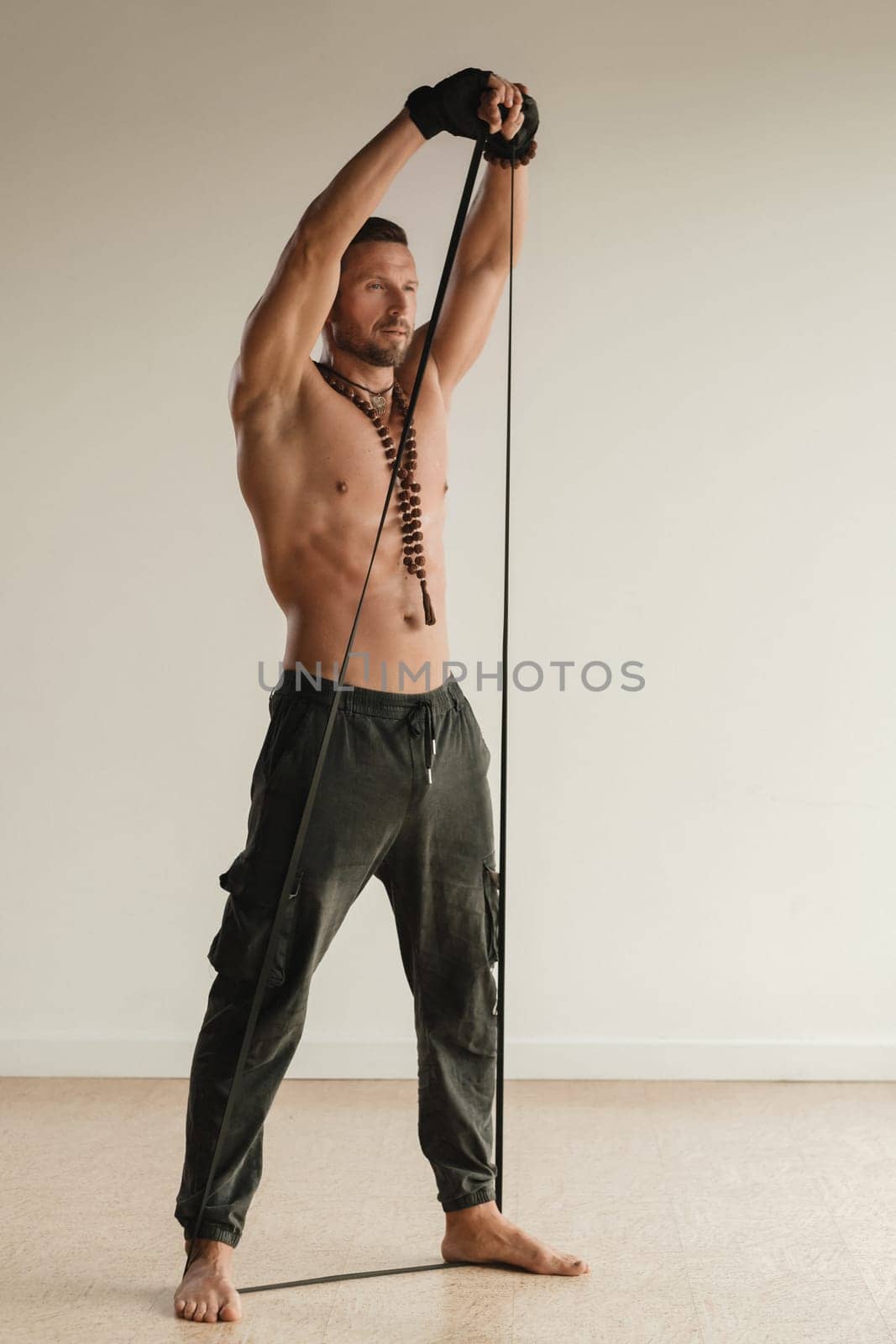 A man with a naked torso is engaged in strength fitness using a rubber loop indoors by Lobachad