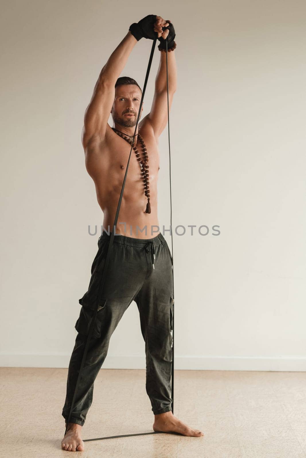 A man with a naked torso is engaged in strength fitness using a rubber loop indoors by Lobachad