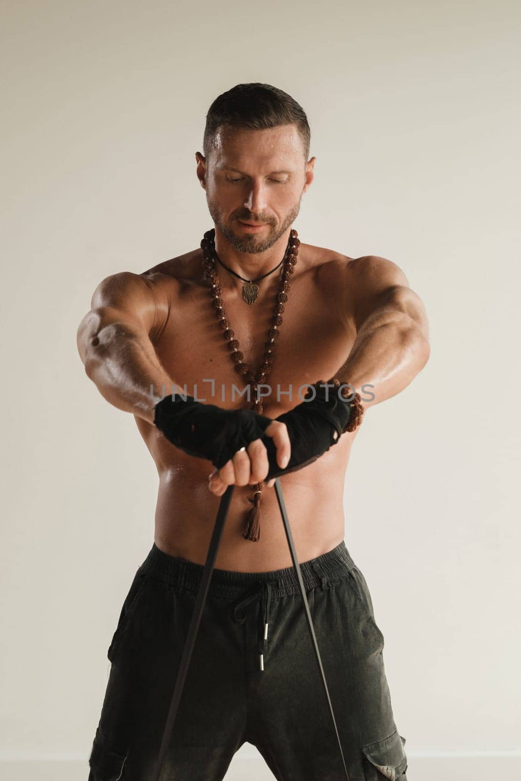 A man with a naked torso is engaged in strength fitness using a rubber loop indoors.