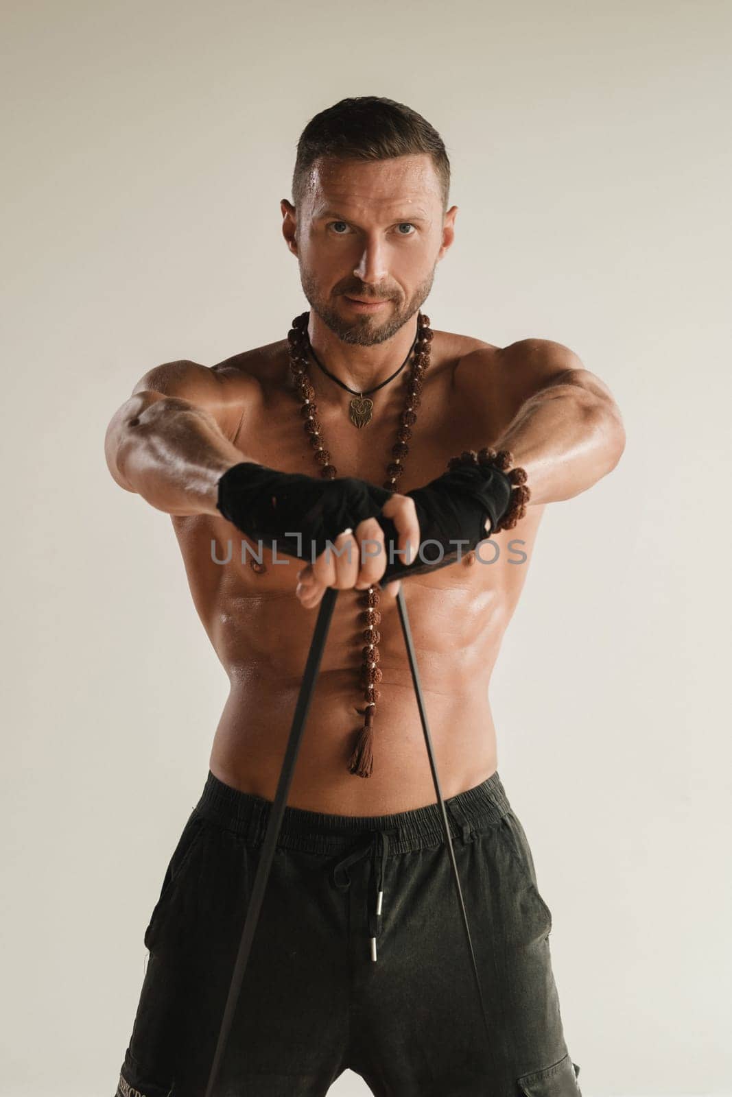 A man with a naked torso is engaged in strength fitness using a rubber loop indoors by Lobachad